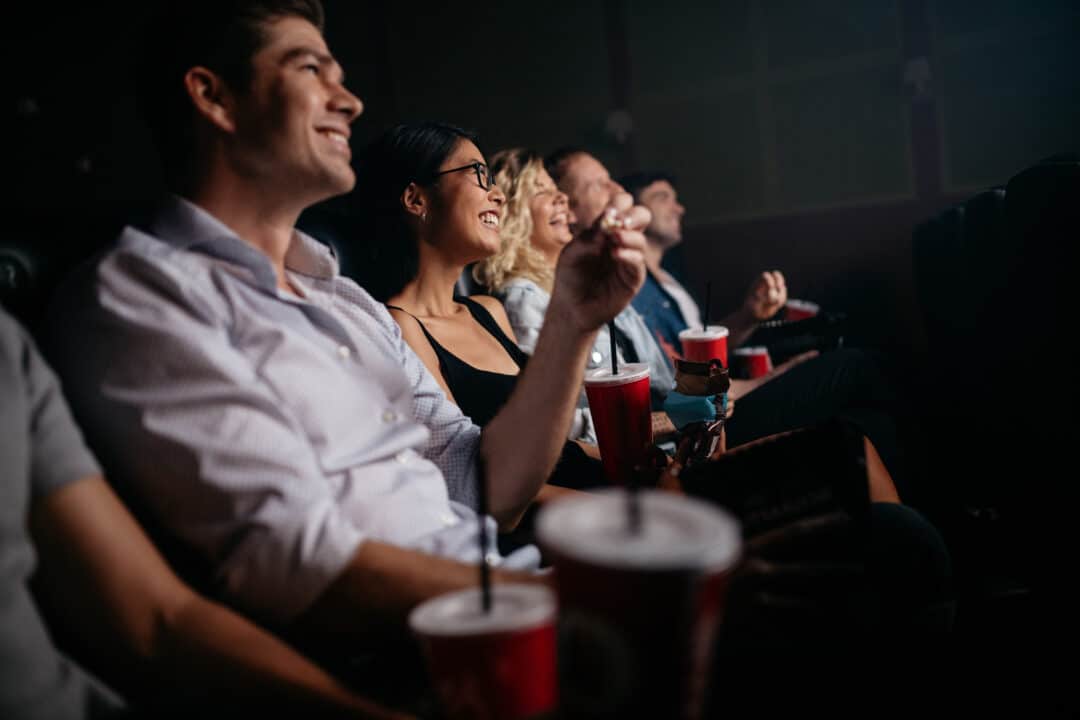 Group of people in theater with popcorn and drinks. Young friends watching movie in cinema.